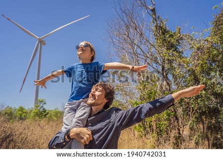 Alternative energy, wind farm and happy time with your family. Happy father carrying his son on shoulders is on vacation and escape to nature. Father carrying son on shoulders and waving their arms