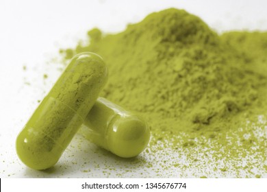 Alternative medicine, herbal pain management and opioid withdrawal treatment concept theme with a pile of green kratom powder and capsules or pills isolated on white background