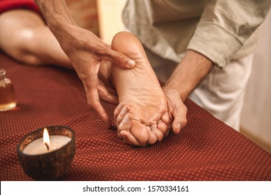 Alternative Medicine Salon Therapist Healing Woman Doing Ayurvedic Massage With Lighted Aroma Candle On Foot Pressing On Meridian Close-up