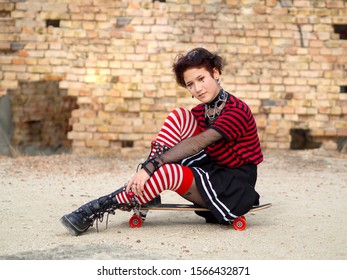 Alternative Punk Girl Sitting On A Skate Board On A Brick Wall Background. Goth Dark Teen Concept