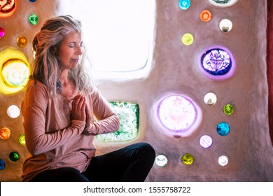 Alternative relaxed caucasian woman meditating and relaxing at home in yoga balance position -  artistic wall with coloured glass in background