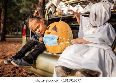 Alternative safe celebration. Cute kids celebrating Halloween party in the trunk of car with spider net, ghosts, carved pumpkin in medical mask for fun and other decoration, autumn outdoor