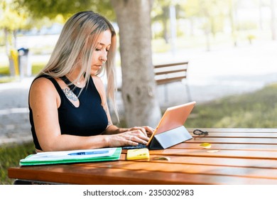 Alternative student taking notes with a tablet on a bench in college.