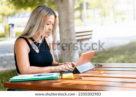 Alternative student taking notes with a tablet on a bench in college.