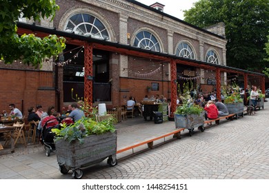 Altrincham, Cheshire/UK - July 6 2019: View Of The Entrance To Altrincham Indoor Market Place On Shaw's Road. People Enjoying Shopping And Food. Brick Building With Distinctive Arched Windows.