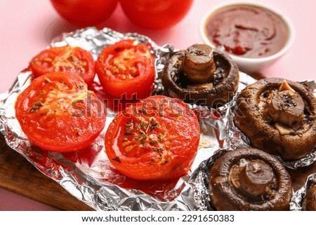 Aluminium foil with tasty baked mushrooms and tomatoes on pink background, closeup