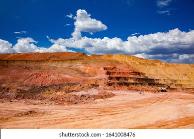 Aluminium ore quarry. Quarry steps of various colors of minerals. Bauxite clay open-cut mining. Excavator loading quarry dump truck (right). On the deep blue sky with white clouds. 