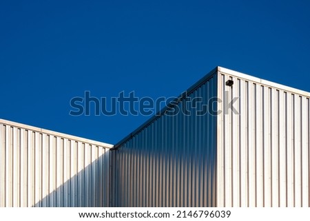 Aluminium Warehouse Building Wall of Industrial Factory against blue clear Sky background with light reflection on surface