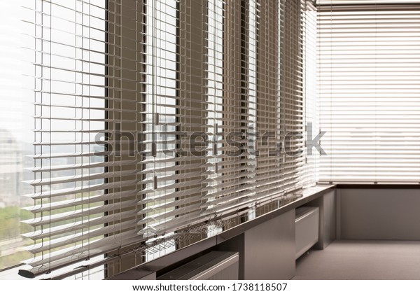 Aluminum blinds. Made from metal. Venetian\
blinds closeup on the window. Silver color. City landscape is in\
the background.