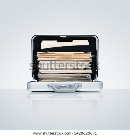 Aluminum briefcase with ambitious stack of files and folders on cool grey aluminum surface with subtle reflection