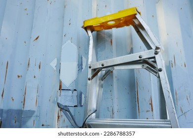 Aluminum folding ladder damaged (A-Type) is leaning against a container wall on construction site.                    