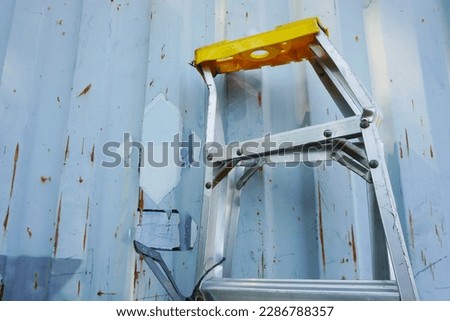 Aluminum folding ladder damaged (A-Type) is leaning against a container wall on construction site.                    