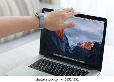 Alushta, Russia - July 30, 2016: Apple Watch In Man Hand Open MacBook Pro With Wallpaper MacOS Sierra On The Screen. Apple Watch And Macbook Pro Was Created And Developed By The Apple Inc.