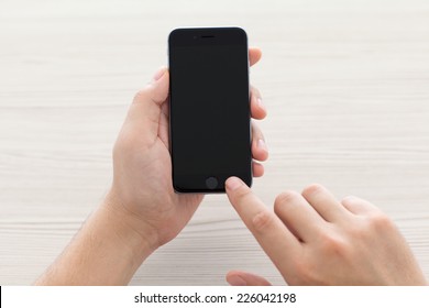 Alushta, Russia - October 23, 2014: Man Switch On The New IPhone 6 Space Gray Holding It Over The Table. IPhone 6 Was Created And Developed By The Apple Inc.