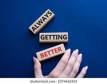 Always getting better symbol. Wooden blocks with words Always getting better. Beautiful deep blue background. Businessman hand. Business and Always getting better concept. Copy space.