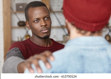 I'm always here for you. Indoor shot of warm-hearted young African American man showing compassion to unrecognizable male, patting him on shoulder while trying to comfort and reassure his best friend