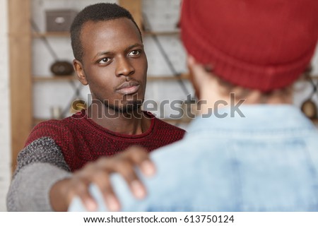 I'm always here for you. Indoor shot of warm-hearted young African American man showing compassion to unrecognizable male, patting him on shoulder while trying to comfort and reassure his best friend