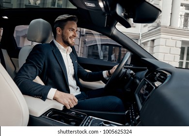 Always In A Hurry. Handsome Young Man In Full Suit Smiling While Driving A Car