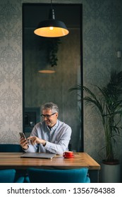 Always On Line With His Business Partners. Senior Man Using Smartphone In Cafeteria