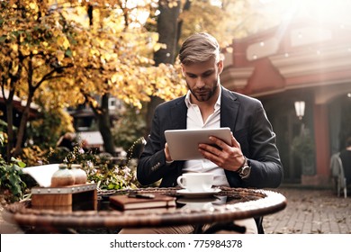 Always online. Good looking young man in smart casual wear using digital tablet while sitting in restaurant outdoors