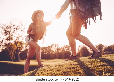 Always ready to help. Man with backpack helping woman to climb the hill while holding her hand  - Powered by Shutterstock - Get 15% off with code: PIKWIZARD15