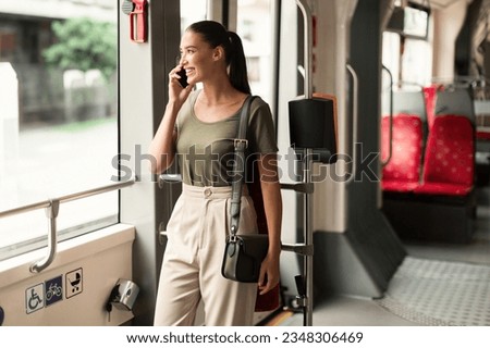 Always In Touch. Smiling Woman Chatting In Tram, Commuting Engaged in Phone Call Inside Modern Train. Passenger Communicating And Enjoying Public Transportation While Traveling to Work