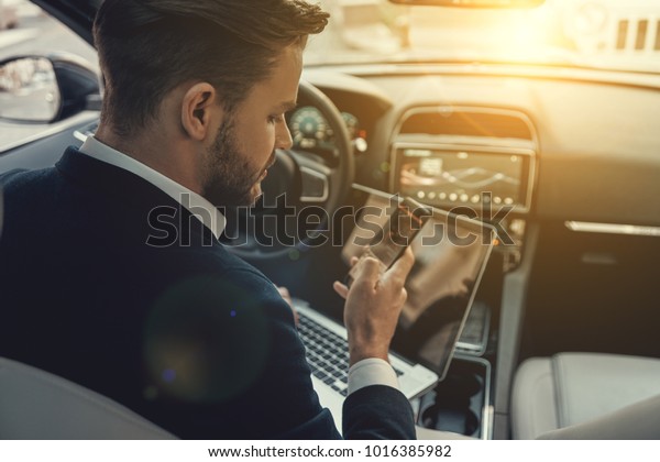 Always in touch. Top rear\
view of young man in formalwear using his smart phone while sitting\
in the car