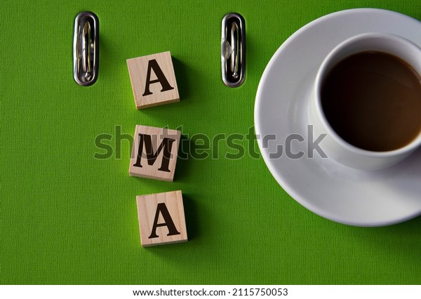 AMA (Ask me\
anything) - acronym on wooden cubes against the background of a\
green folder and a cup of\
coffee.