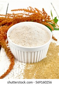 Amaranth flour in white bowl, seeds scattered on the table, brown flower with leaves on the background of wooden boards