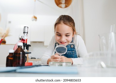 Amased little girl doing home science project, looking through magnifying glass. She has glass chemical equipment and microscope - Powered by Shutterstock