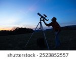 Amateur astronomer looking at the evening skies, observing planets, stars, Moon and other celestial objects with a telescope.