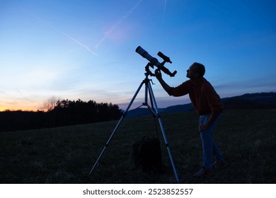 Amateur astronomer looking at the evening skies, observing planets, stars, Moon and other celestial objects with a telescope.