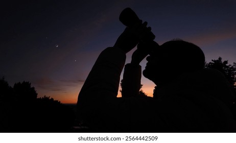 Amateur astronomer looking at the evening skies, observing planets, stars, Moon and other celestial objects with binoculars.
