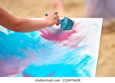 Amateur painter drawing picture on white canvas at outdoor art workshop. Woman artist hands with paintbrush painting new picture, outdoor art exercise, painting performance