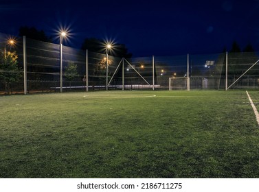 An amateur soccer field illuminated at night. A small football field lit by lanterns in the evening. Green football field illuminated at night. Soccer field in night with spotlight - Powered by Shutterstock