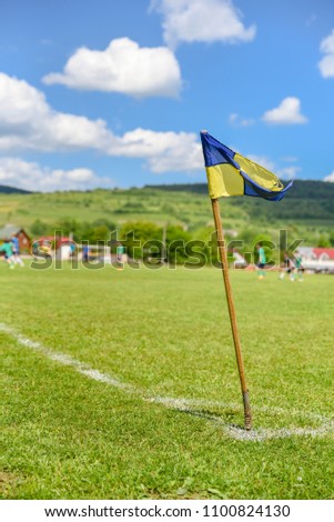 Amateur soccer field, retro corner flag on the foreground, football players are fighting for the ball on the background. Stories about rural life in Ukraine