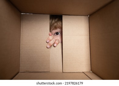 Amazed adorable little boy peeking inside gift box, unpacking present with funny astonished expression, impatient child unboxing surprise. Close up eyes looking.