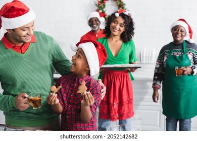 amazed african american boy in santa hat showing christmas cookies to dad with cup of orange cinnamon tea