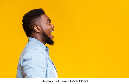 Amazed African American Man Shouting At Free Space With Excitement, Yellow Studio Background, Side View