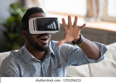 Amazed African American young man wearing virtual reality glasses touch air using AR interface, excited biracial millennial male in new digital VR goggles have fun playing, new technology concept