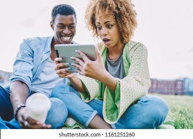 Amazed african american young woman together with surprised boyfriend shocked with incoming notification on touch pad device.Excited dark skinned friends received happy news on modern tablet