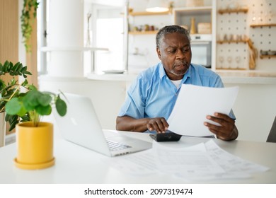 Amazed African Pensioner Sitting At Home And Looking At Bills He Has To Pay. He Is Paying It Online Over A Laptop.