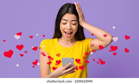 Amazed Asian Woman Holding Smartphone, Looking At Device Screen With Excitement, Standing With Open Mouth Over Purple Studio Background With Red Hearts, Emotionally Reacting To Love Message, Collage