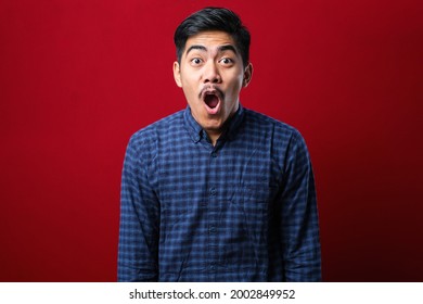 Amazed Asian Young Man With Open Mouth And Bulging Eyes Looking At Camera Isolated Red Background