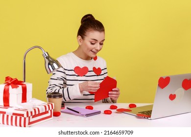 Amazed Astonished Young Woman Opening Envelope And Reading Letter, With Surprised Expression, Sitting At Workplace With Laptop. Indoor Studio Studio Shot Isolated On Yellow Background.