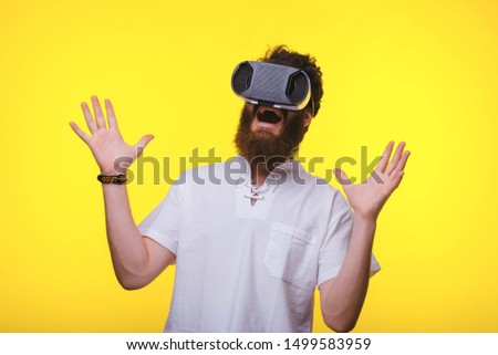 Amazed bearded guy using VR glases, stnading over yellow wall 