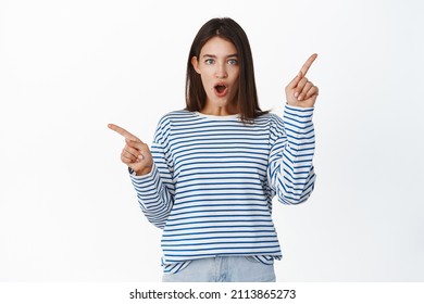 Amazed Brunette Girl Gasp And Say Wow, Pointing Sideways, Showing Two Choices, Ways, Standing Over White Background