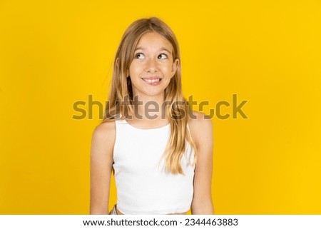 Amazed Caucasian kid girl wearing white T-shirt over yellow background bitting lip and looking tricky to empty space.