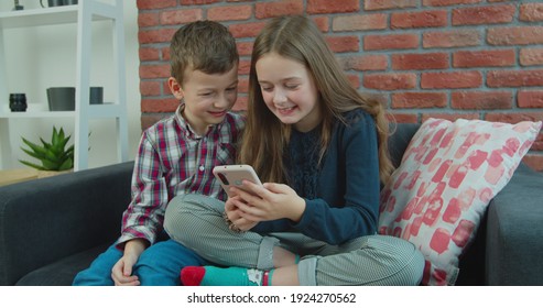 Amazed Children Watching Smart Phone, Happy Young Kid Using Smartphones Together, Smiling Beautiful Having Fun With Phones, See Funny Video In Social Network, Playing Mobile Games, Reading Good News.