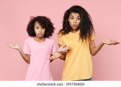 Amazed Confused African American Young Woman And Little Kid Girl Sisters In Casual T-shirts Looking Camera Spreading Hands Isolated On Pastel Pink Color Background Studio Portrait. Family Day Concept